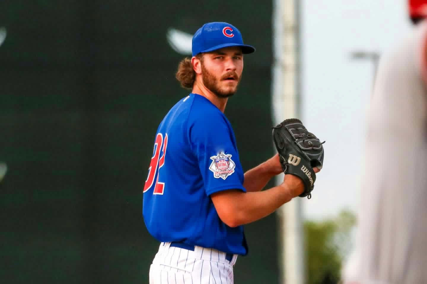 Wilson Cunningham holding a baseball glove in a pitching stance, wearing a Cubs uniform and looking to home plate during a game