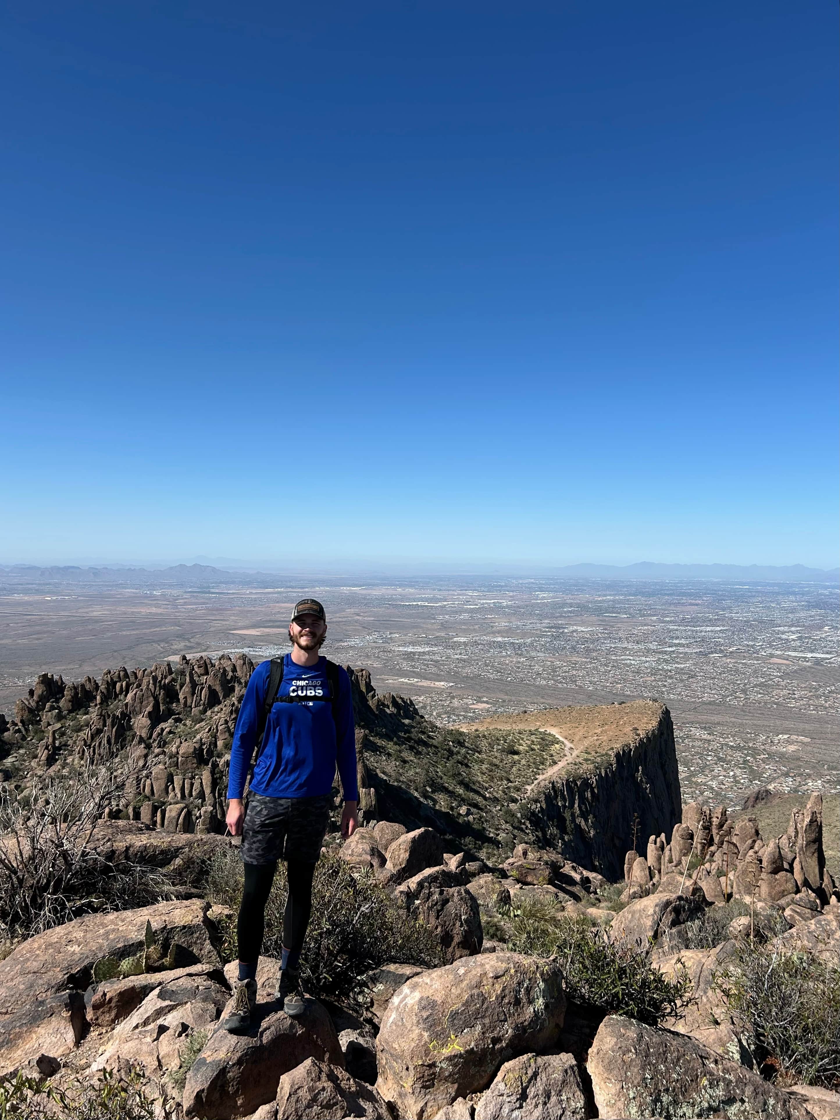 Hiker standing on summit with wide desert landscape and mountain ridges in the distance at Flatiron, Arizona