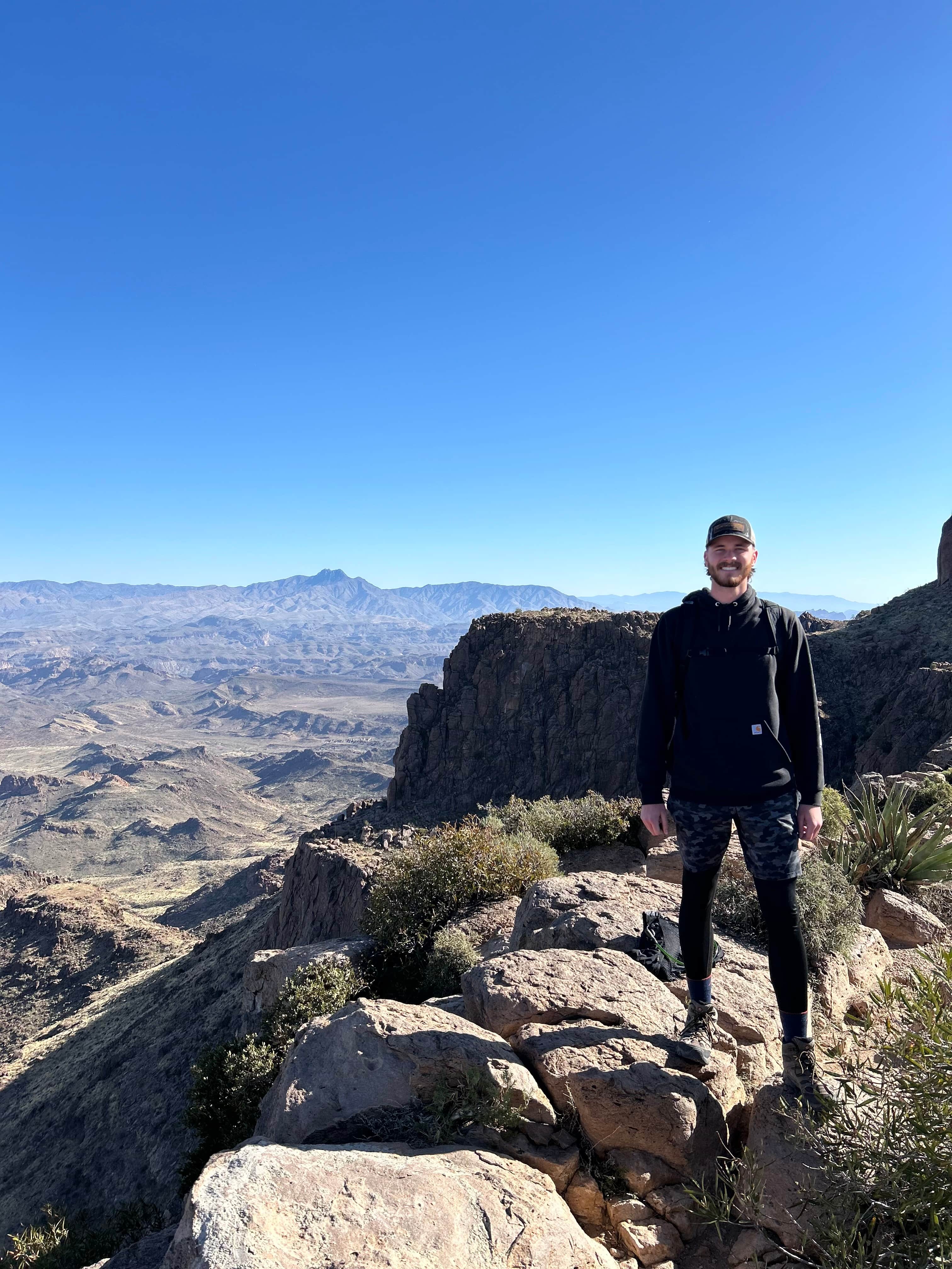 Hiker standing on a rocky ledge with expansive desert and mountain views from Flatiron in Arizona